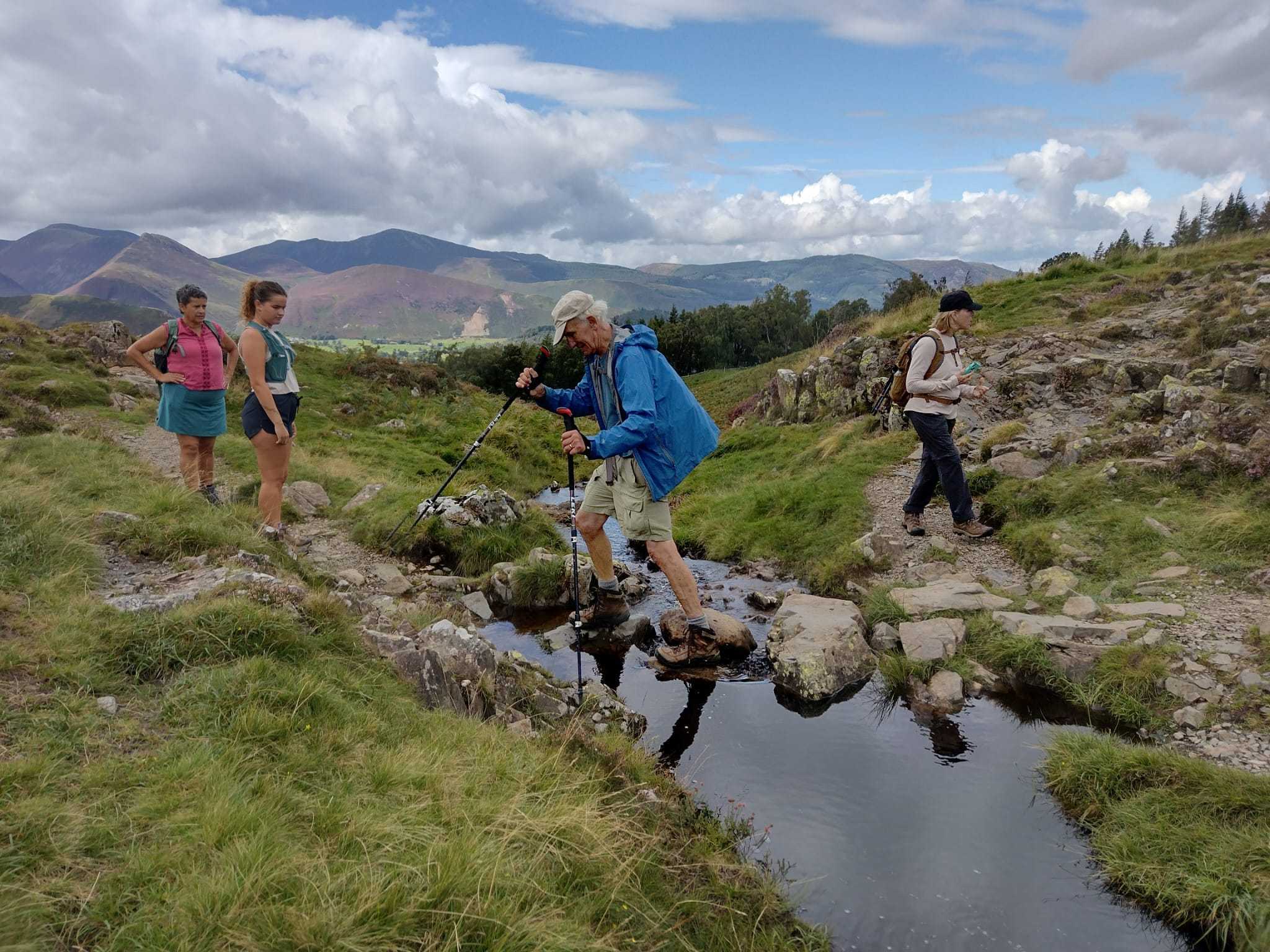 Hikers crossing a stream on stepping stones on the fells above Derwentwater